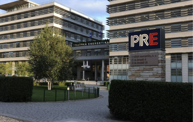 Velká patrová prosklená budova Pražské energetiky, která stojí za značkou Enkidoo. Před budovou je park se stromky a fontánou.